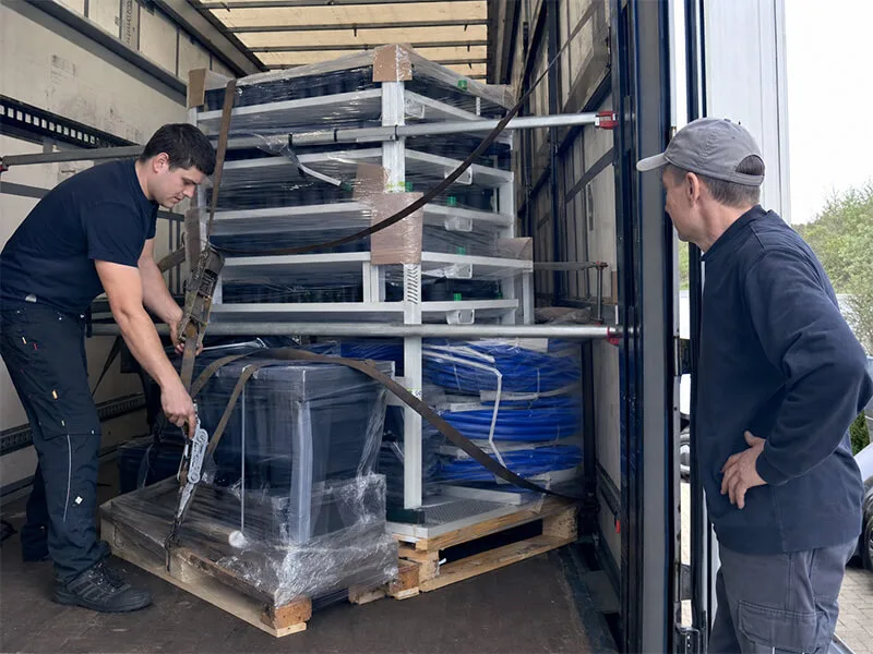 Workers securing hydroponic growing racks with straps inside a delivery truck